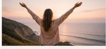 Woman with arms raised at ocean sunset on a cliff